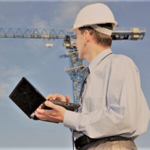 Engineer with laptop against crane